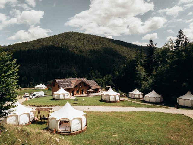 Глемпінг Перестанок: білі намети на галявині біля дерев’яного будинку серед гір